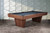 The Preakness Slate Pool Table by Doc & Holliday is captured here in a professionally styled studio environment, emphasizing its soft-rounded corners and bold pedestal base. The warm wood finish and sculpted silhouette are perfectly lit, highlighting the table’s refined form and luxury appeal. Studio-staged to resemble a high-end interior, this hero image showcases why the Preakness is a Sawyer Twain exclusive for design-forward spaces.