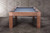 This image provides a full-width view of the Alta Slate Pool Table’s rectangular Parsons-style legs, finished in warm Honey Ash. The wide-set base emphasizes the table’s architectural symmetry and grounded presence, making it ideal for modern interiors that value clean lines and furniture-grade construction. The sleek ash wood structure brings both stability and subtle elegance to this Sawyer Twain exclusive.