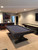 Otis Slate Pool Table in Smokehouse finish by Plank & Hide, featured in a luxury basement bar with warm wood accents and lounge seating; matching Otis Shuffleboard Table shown separately in the same space to highlight coordinated design and rustic-modern styling